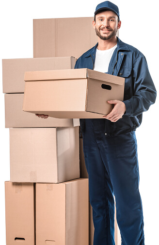 A smiling man wearing a blue uniform and cap stands next to a stack of cardboard moving boxes, holding one box in his arms, suggesting a moving or delivery scenario.