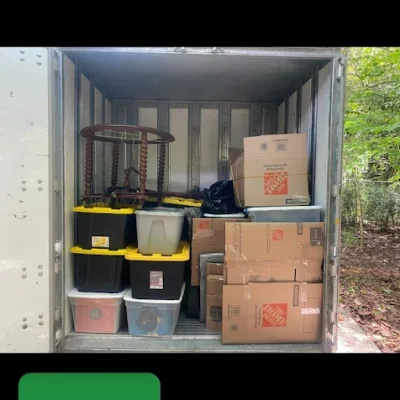 Interior of a moving truck or storage container packed with boxes, bins, and furniture, with a green "Arrived" notification in the bottom left corner.